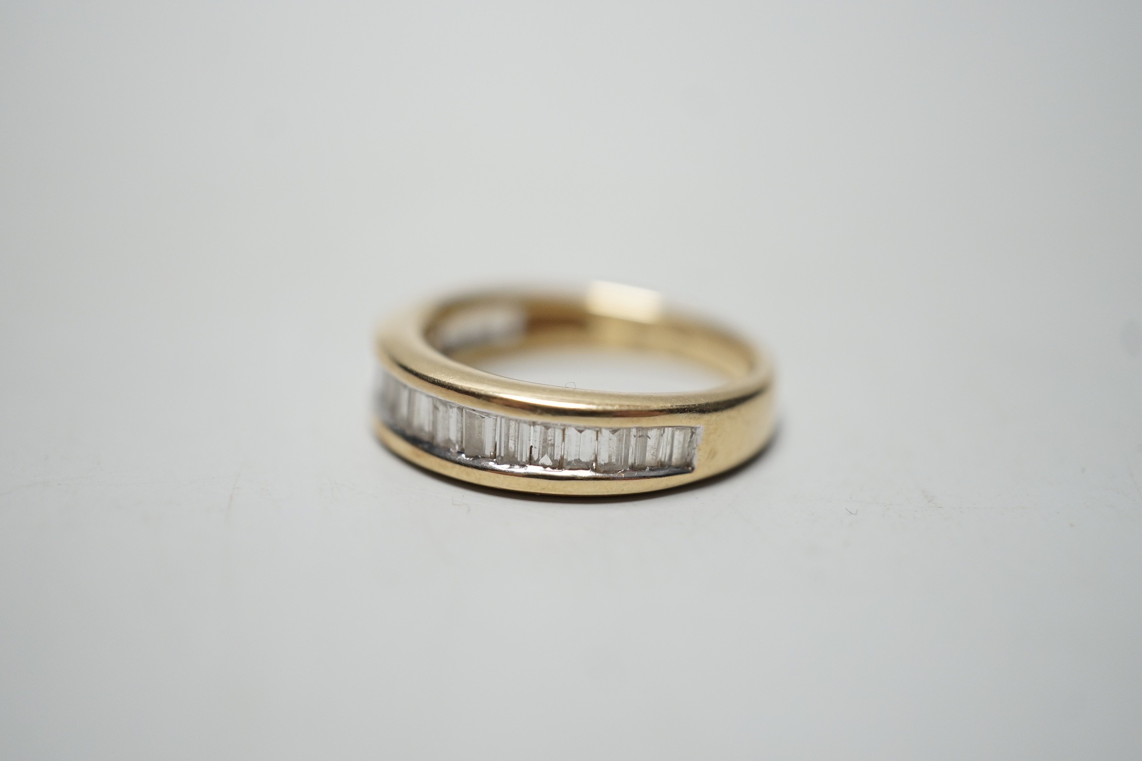 A modern 14k yellow metal and graduated baguette and trapeze cut diamond set half eternity ring, size N, gross weight 4.6 grams.